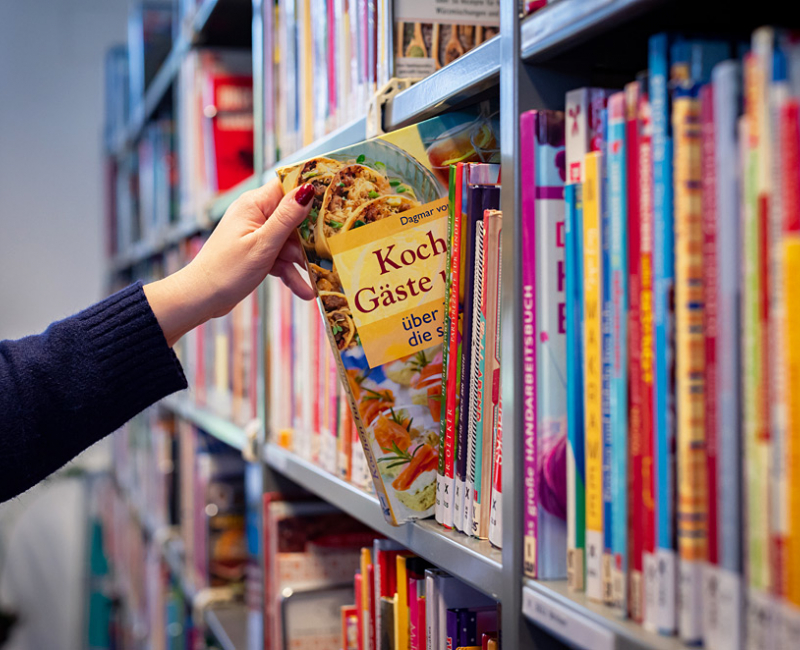 Leser nimmt ein Buch aus dem Regal mit dem Titel - Kochen für Gäste