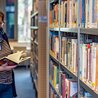 Eine Frau steht vor einem Bücherregal und blättert in einem Buch